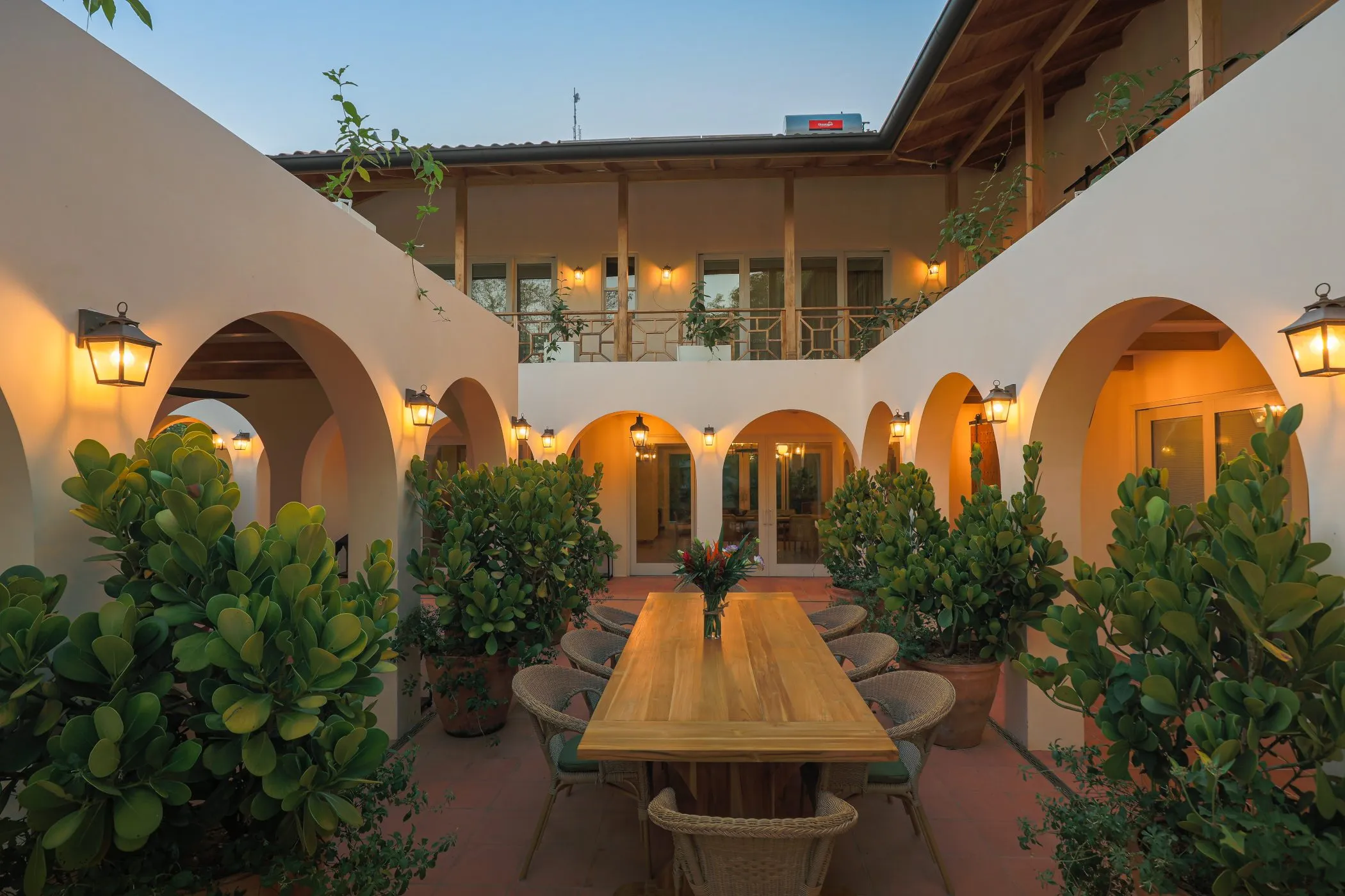 Casa Oceanus villa Mediterranean courtyard with arches and long communal dining table at twilight, Guiones Beach Club, Nosara, Costa Rica