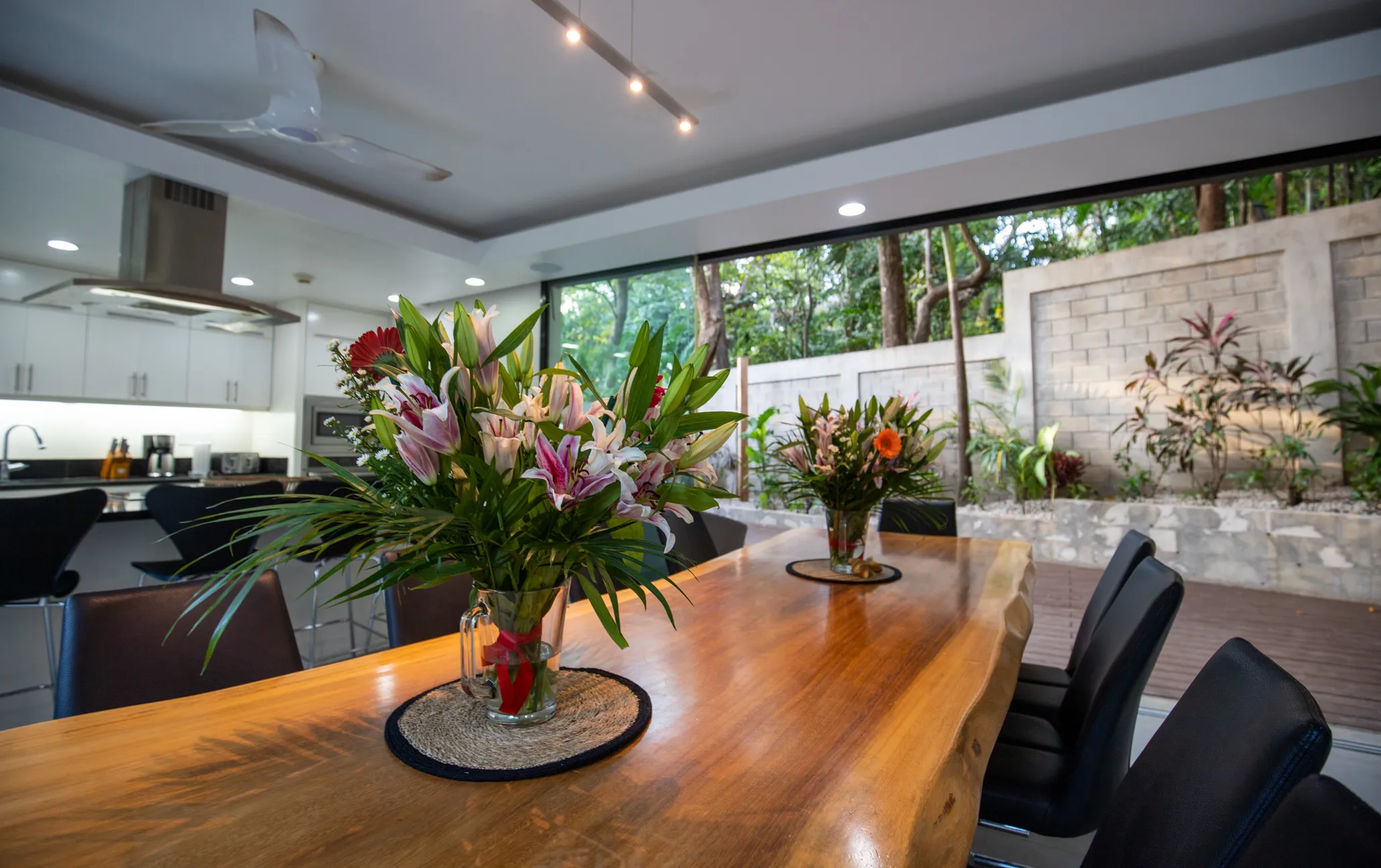 Casa Almendra villa long Guanacaste wood dining table with flower arrangements and kitchen behind, Nosara