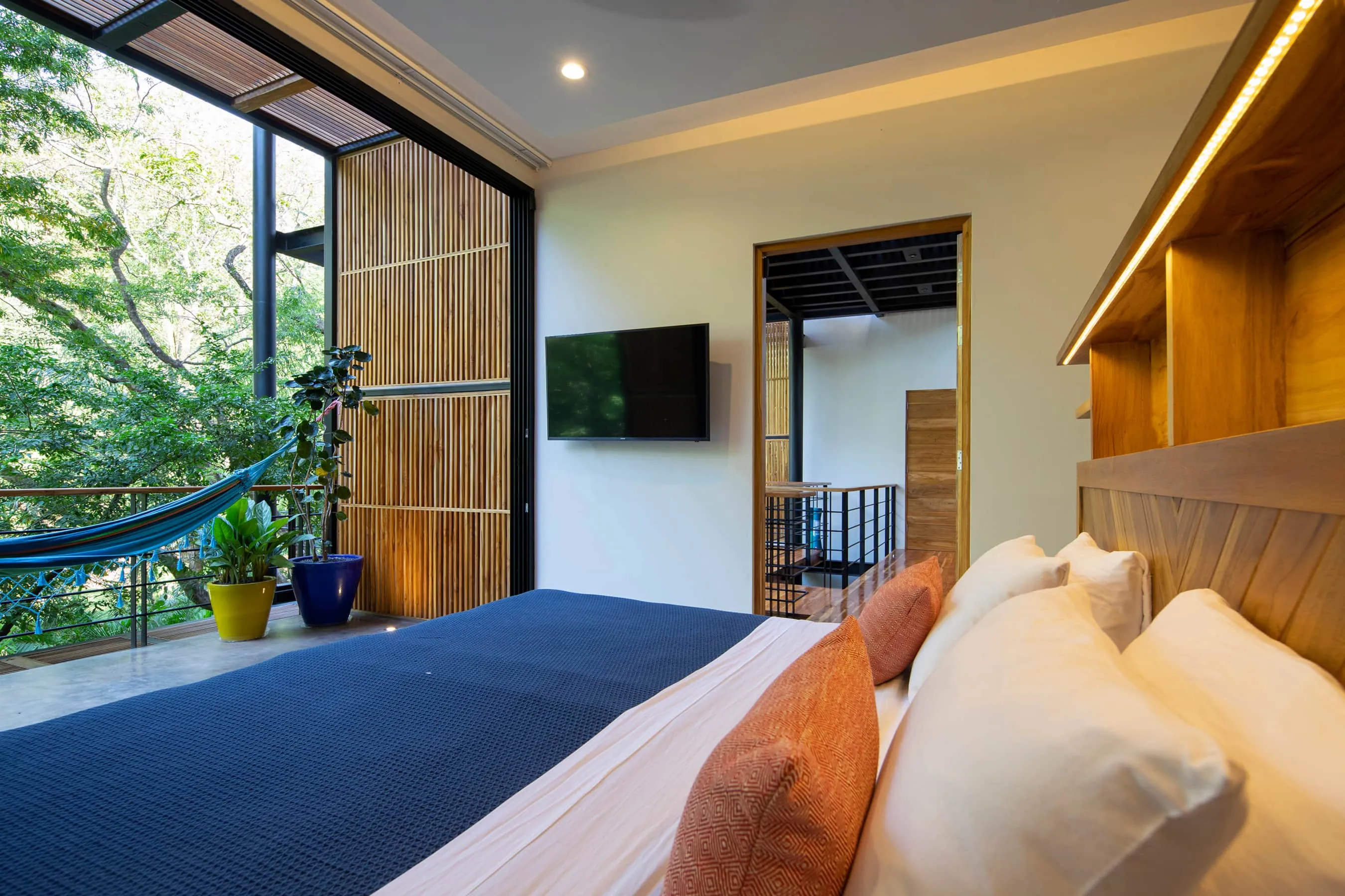 Terrace House villa bedroom with blue bedspread and hammock visible through glass to jungle, Studio Saxe Nosara
